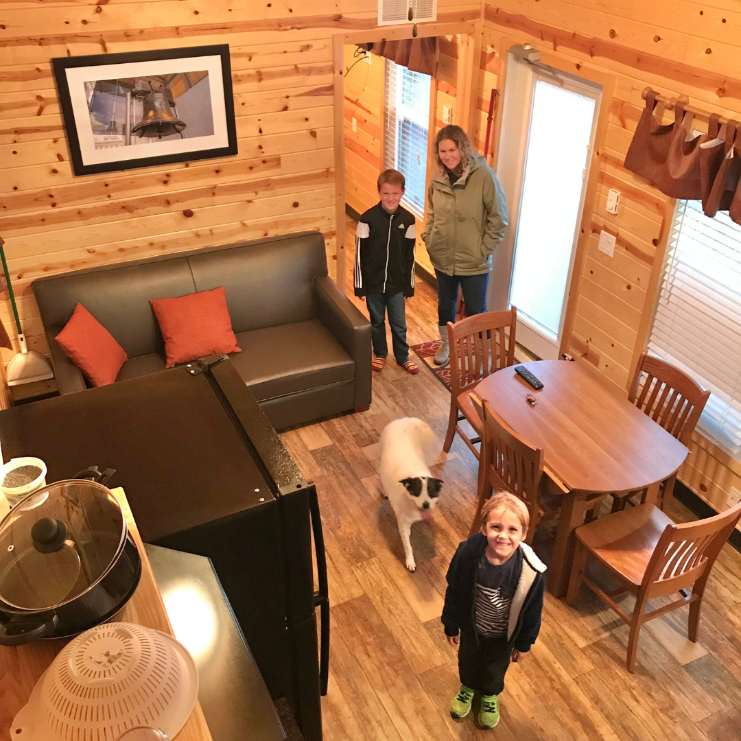 Two boys, a women, and dog inside a camping cabin