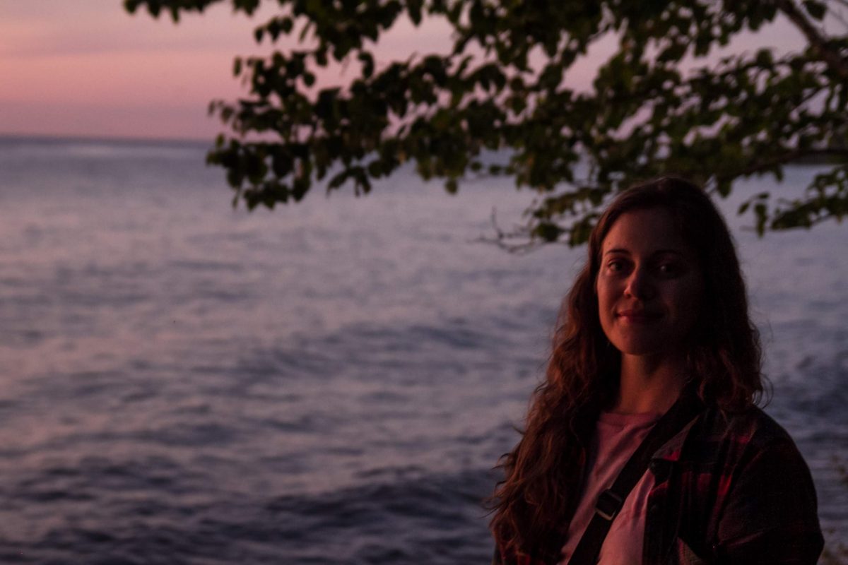 A woman smiles for the camera while the sunsets behind her on Lake Michigan on Fisherman's Island State Park in Northern Michigan.