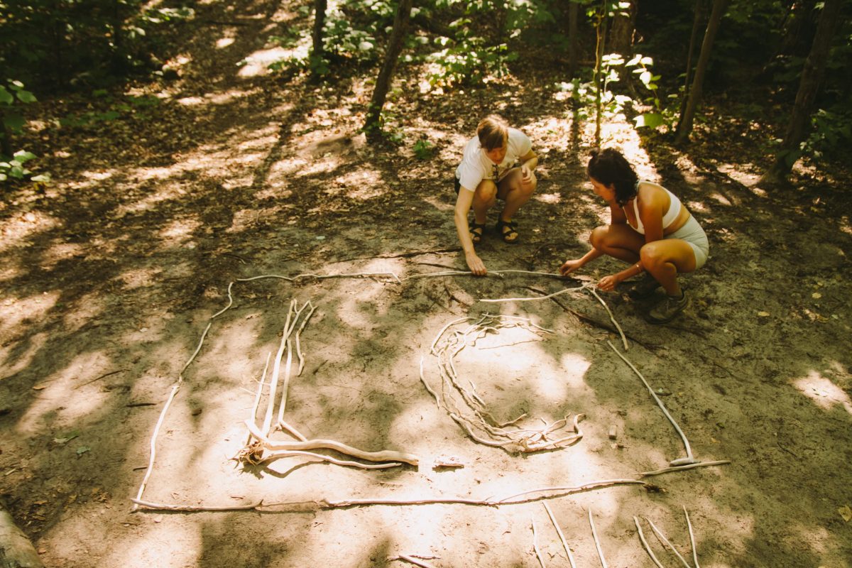 Two women arrange beach wood, spelling out the letters LC, standing for Lady Camping.