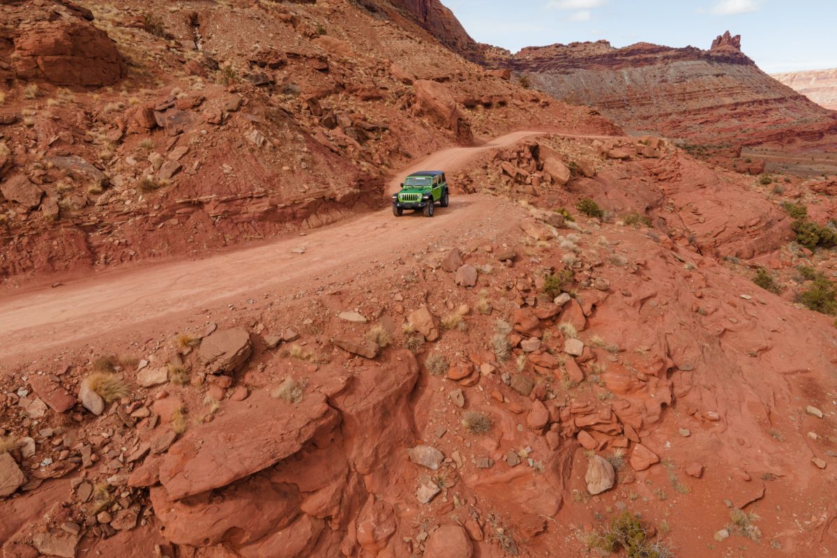 A green jeep rides along the edge of the Gemini Bridges OHV trail in Moab, Utah.