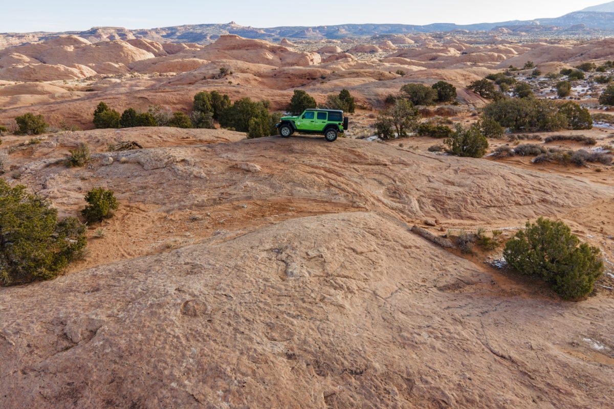 A green jeep sits on top of a sandstone fin on Find & Things trail in Moab, Utah.