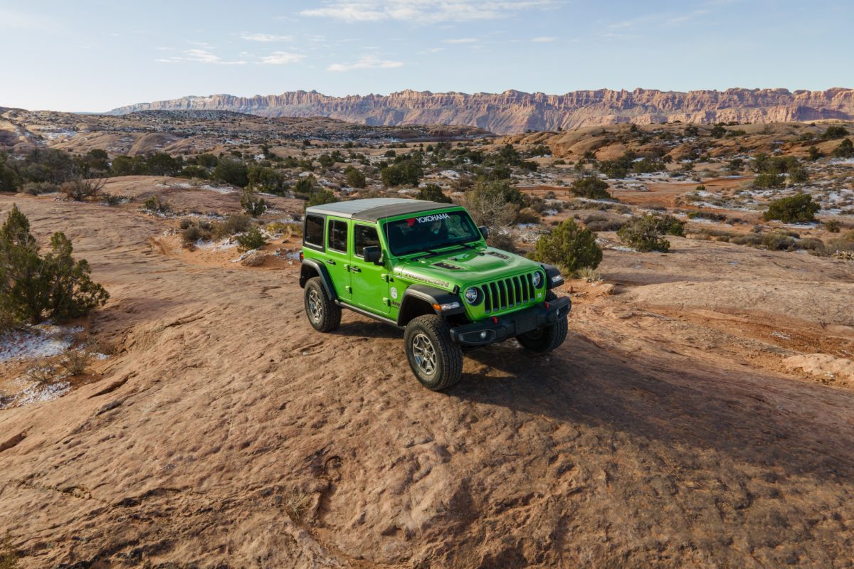 A green jeep sits on top of slickrock on Fins & Things OHV trail in Moab, Utah.