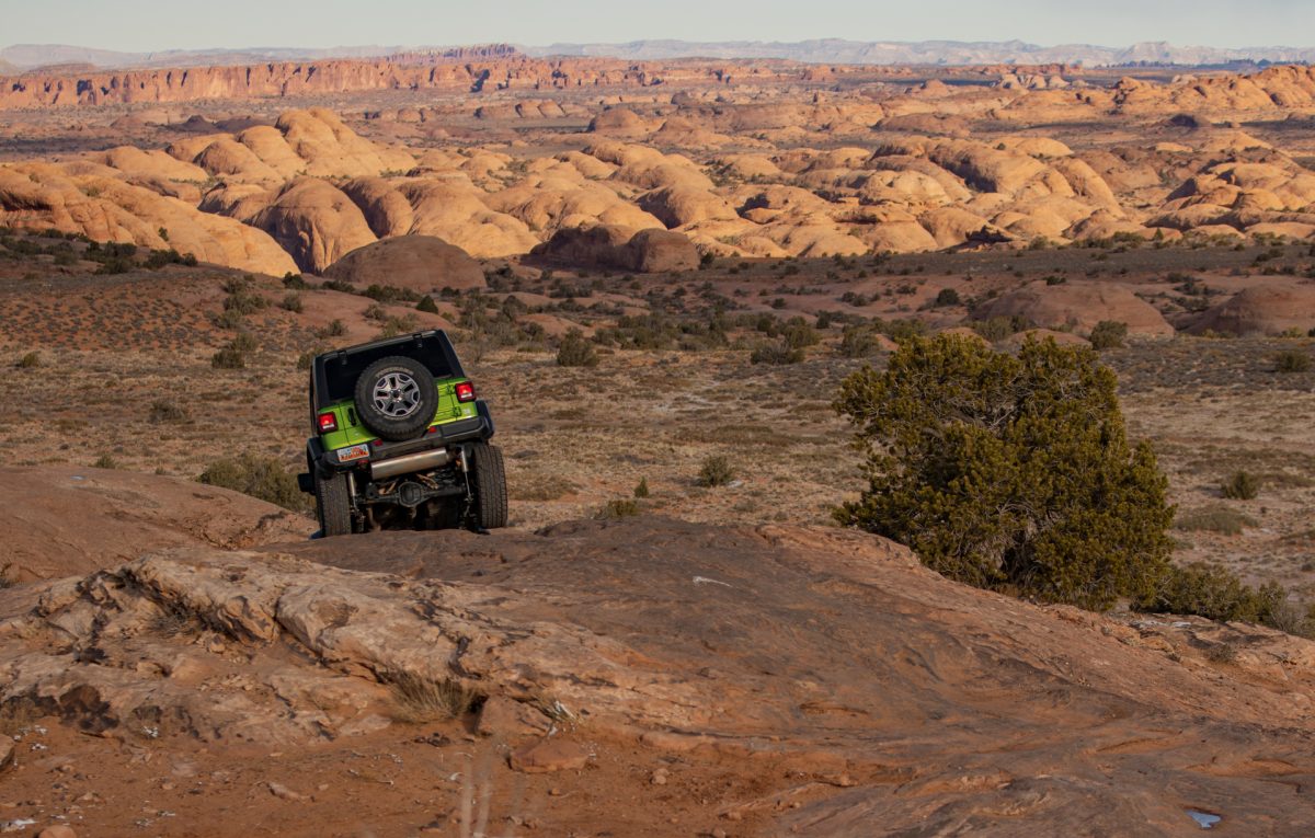 A green jeep goes down a slickrock fin on the Fins & Things OHV trail in Moab, Utah.