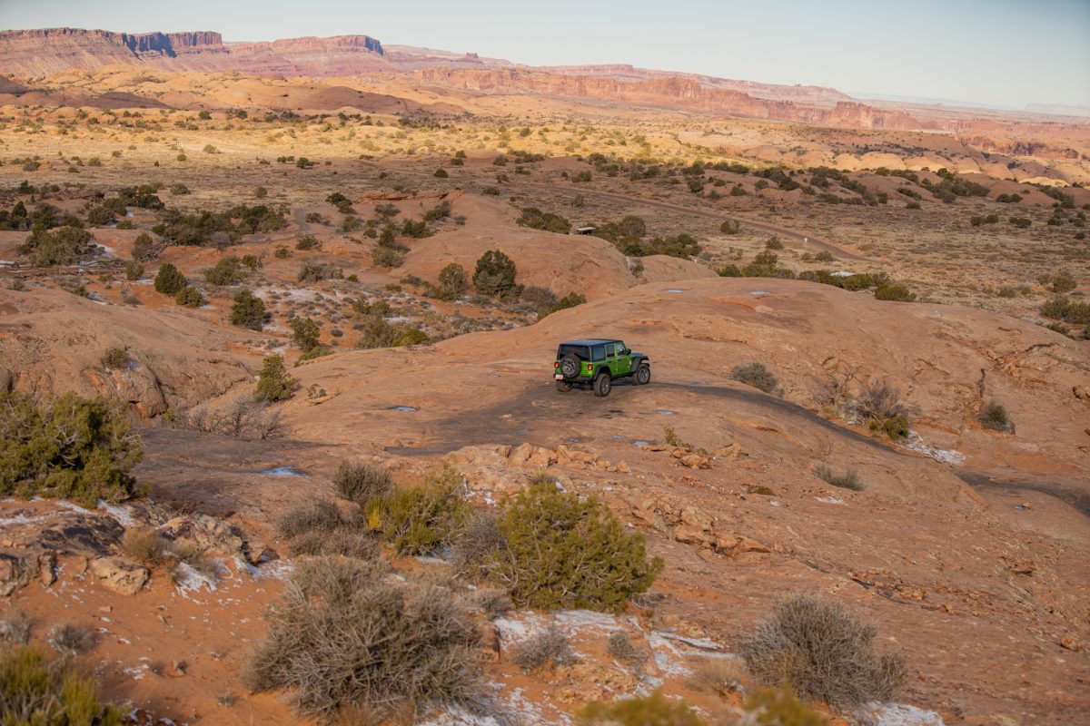 A green jeep drives on top of slickrock at the Fins & Things OHV trail in Moab, Utah.