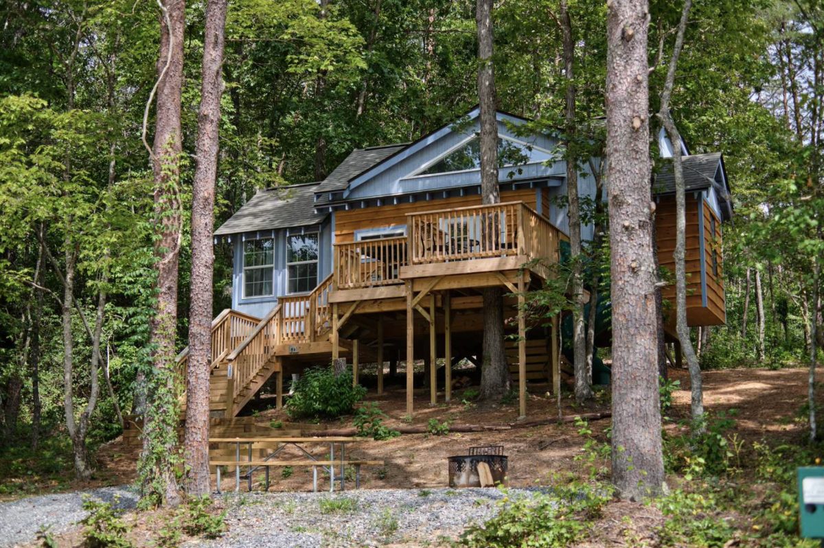 Blue family treehouse in the woods with a picnic table and outdoor fire ring. 