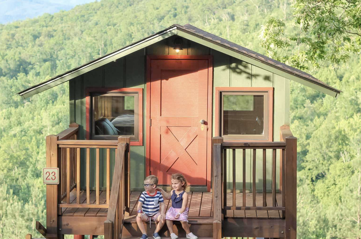 Two children sitting in front of a treetop cabin 