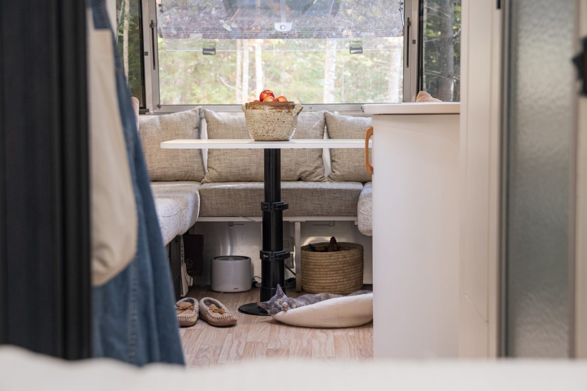 A cat sleeps on a bed on the floor of an RV trailer. On top of the dinette above the cat there is a bowl full of apples.