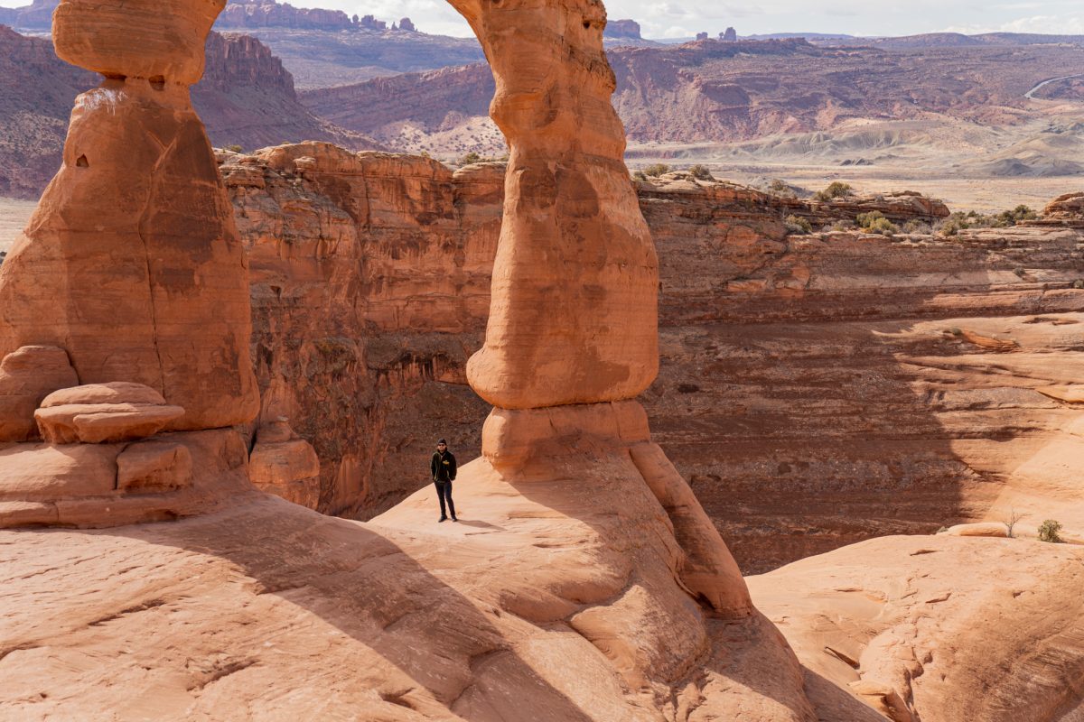 A man stands underneath Delicate Arch at Arches National Park in Utah.