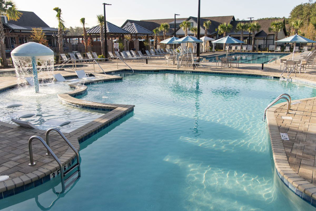 Pool area with palm trees and club house in the background at Carolina Pines RV Resort