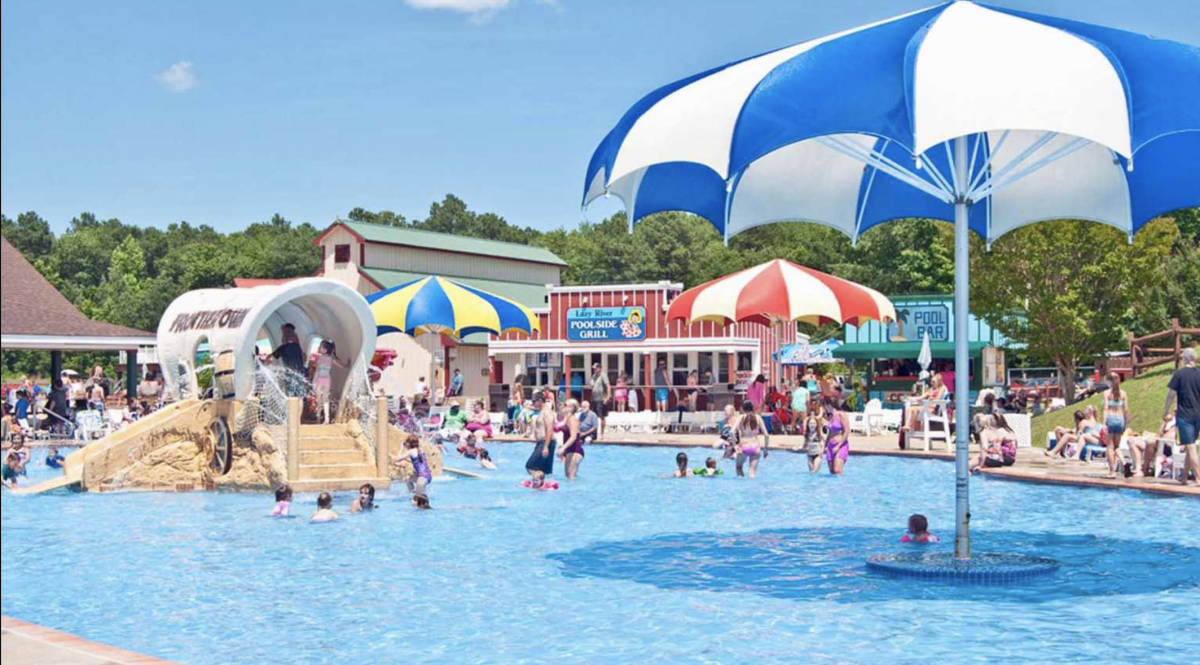 Pool area at Frontier Town RV Resort with giant umbrellas and kids playing in the pool.