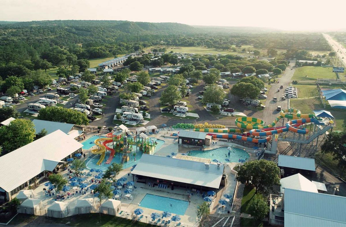 Ariel photo of the pool and waterslides at Jellystone Park Guadalupe River with RVs and mountains in the background.