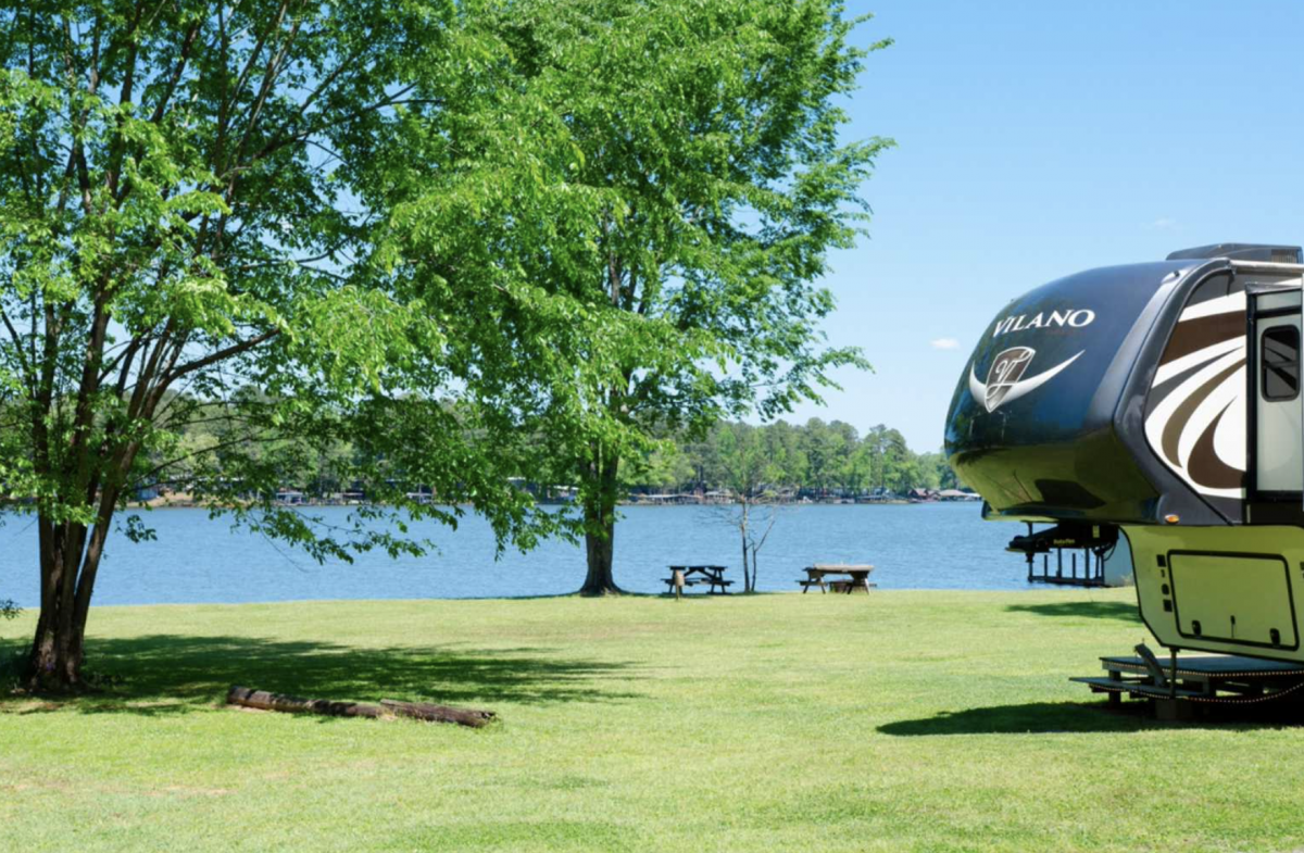 RV parked next to water with 2 picnic tables. 