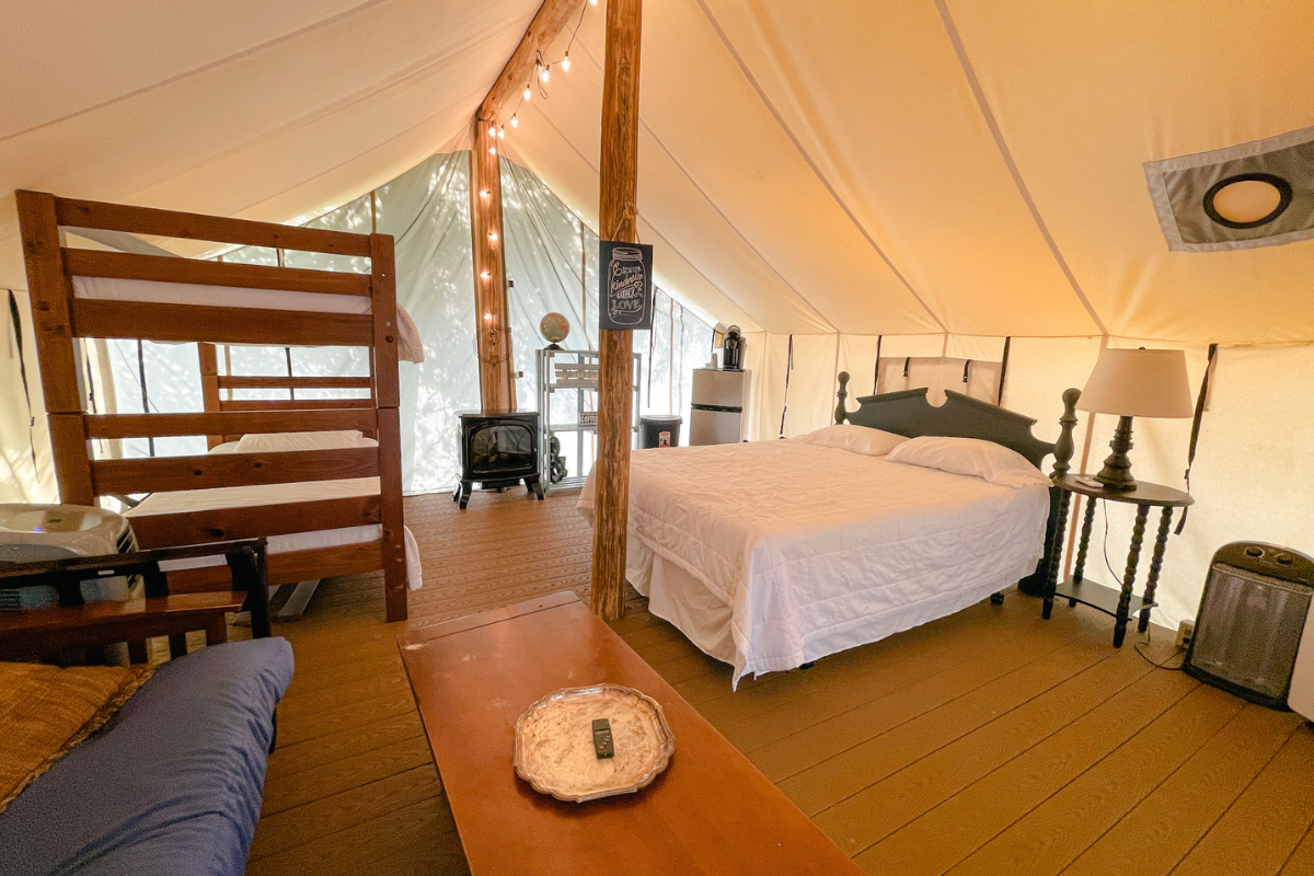 Inside of a glamping tent with a queen bed and bunk beds