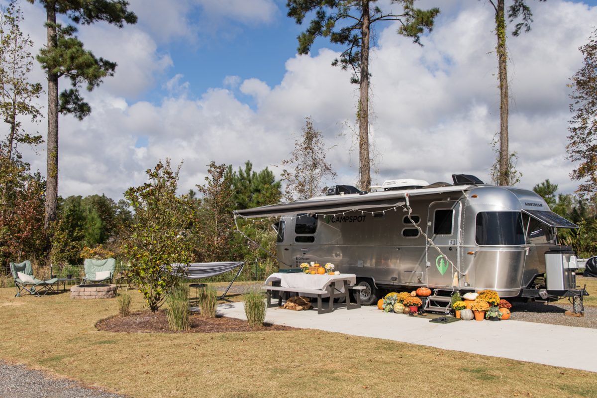 A Campspot Airstream RV sits on an RV site in Carolina Pines RV Resort in Conway, South Carolina. The trailer is decorated with fall pumpkins and decorations.