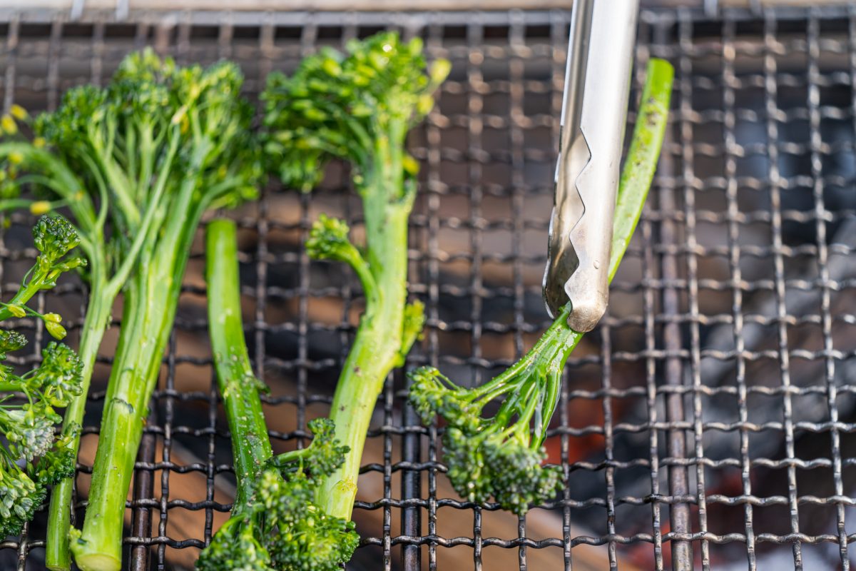 Someone flips over the broccolini on the campfire grate.