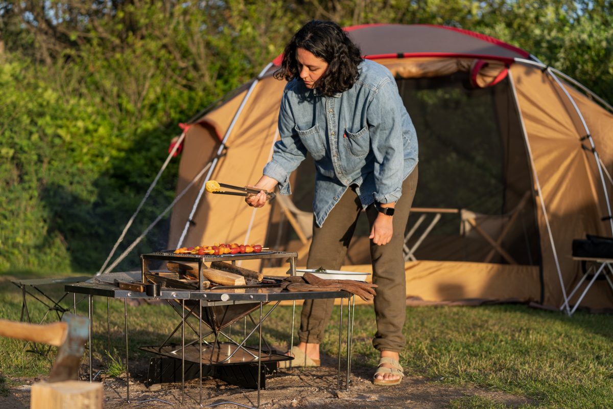 A woman tends to the roasted vegetables while making campfire roasted tomato pasta with burrata and broccolini. 