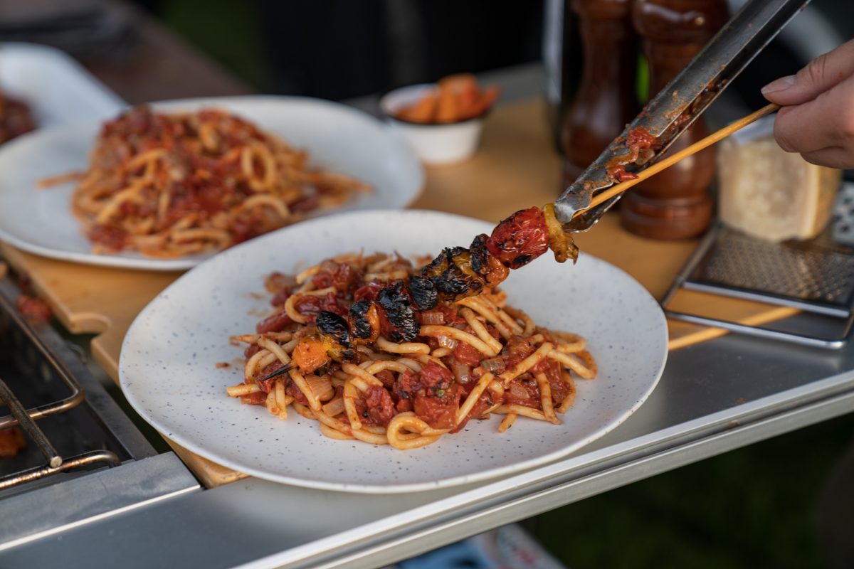 A person places roasted tomatoes on top of pasta.