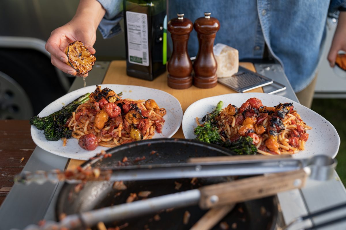 Someone squeezes charred lemons onto two plates of fire roasted tomato pasta with burrata and broccolini. 