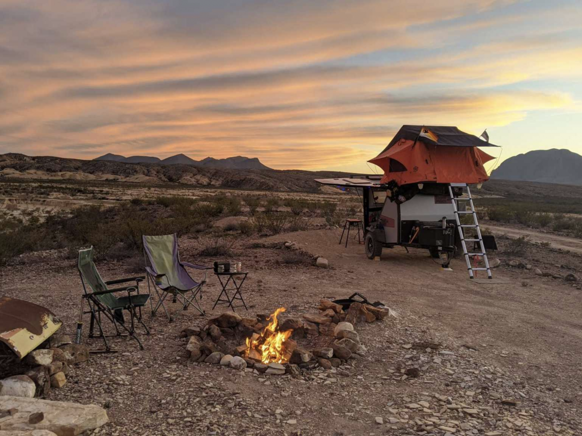 A campsite at Eco-Ranch Rustic Camping Area in Alpine, Texas, with a campfire list and camp chairs set up.