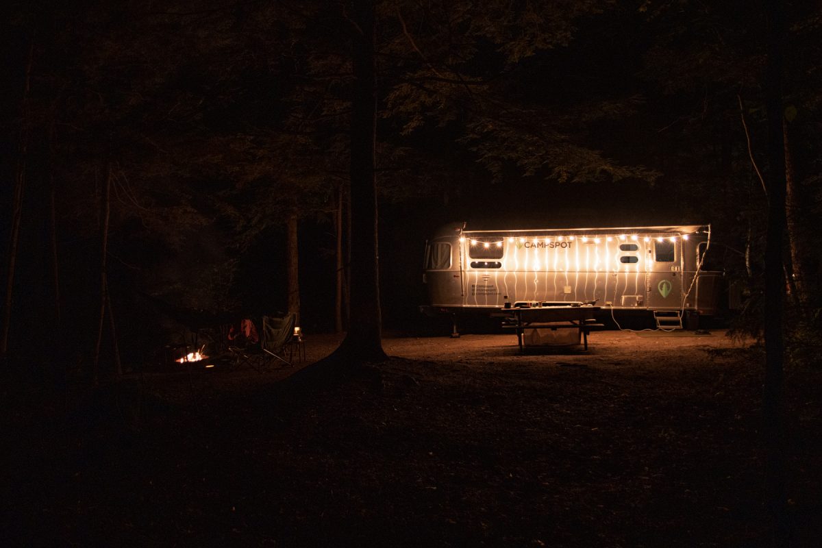 The nighttime depiction of a campsite lit by string lights and a campfire.