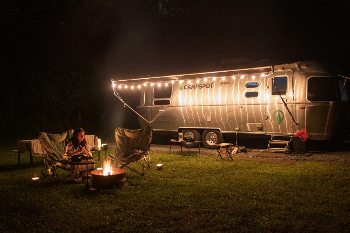 A camper sits and enjoys their campfire in front of their Airstream trailer.