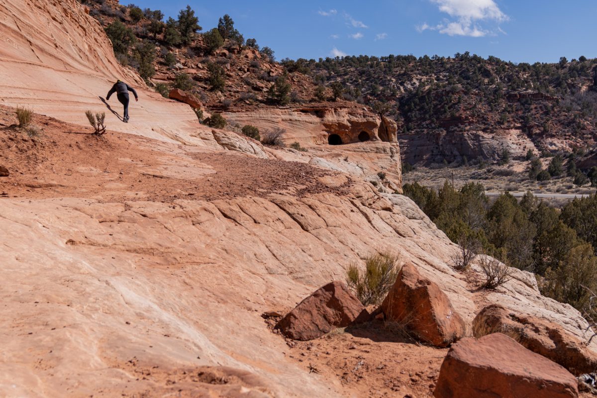 A hiker climbs the sandstone with Sand Caves in the background near Kanab, Utah.