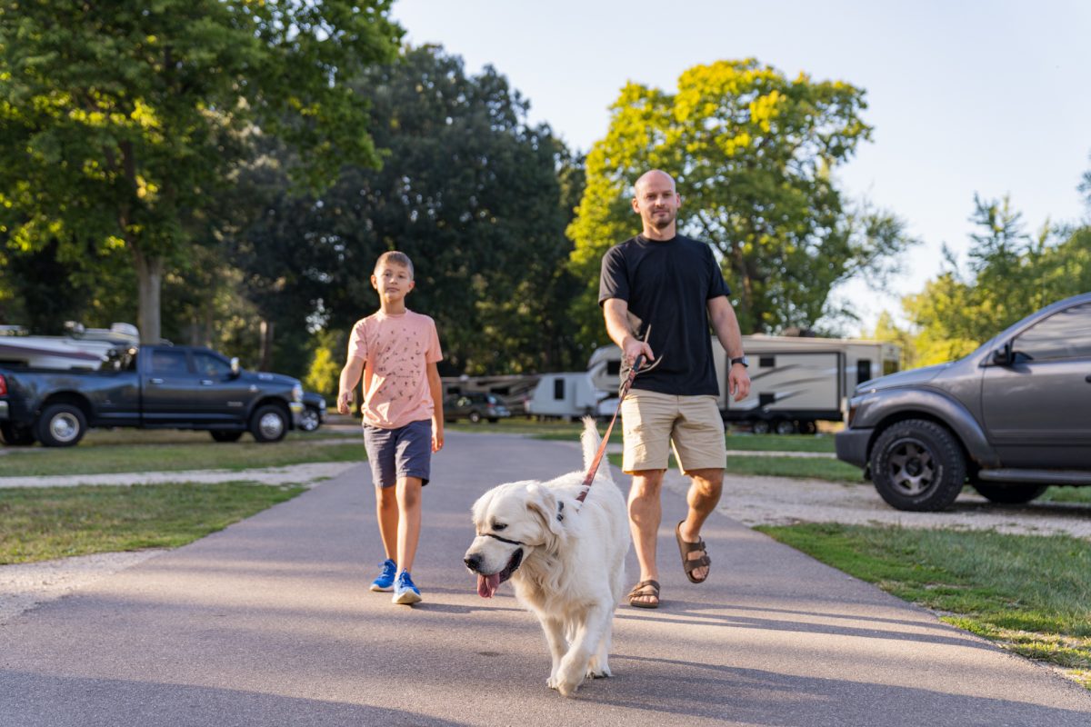 Two campers walking their dog at the campground. Camping with dogs can be a fun way to exercise your dog and get them outdoors.