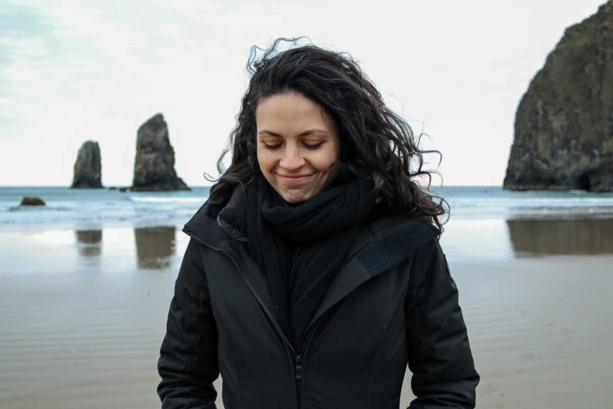 A woman walks Cannon Beach with Haystack Rock and the Needles in the back.