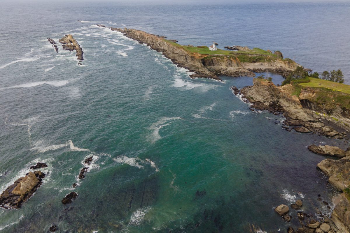 An aerial view of Cape Arago Lighthouse and surrounding rocky reef and terrain at the Cape Arago State Park located near Coos Bay, Oregon.