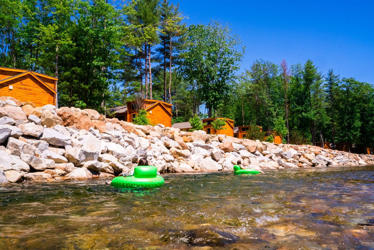 Cabins next to the river with people tubing at Yogi Bear's Park in Glen, NH