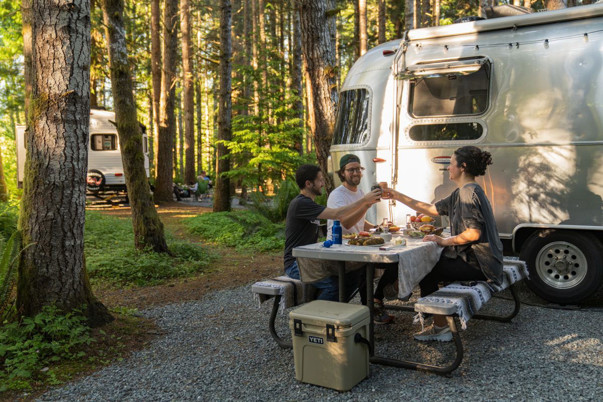 Three people sitting at a campground table next to airstream 