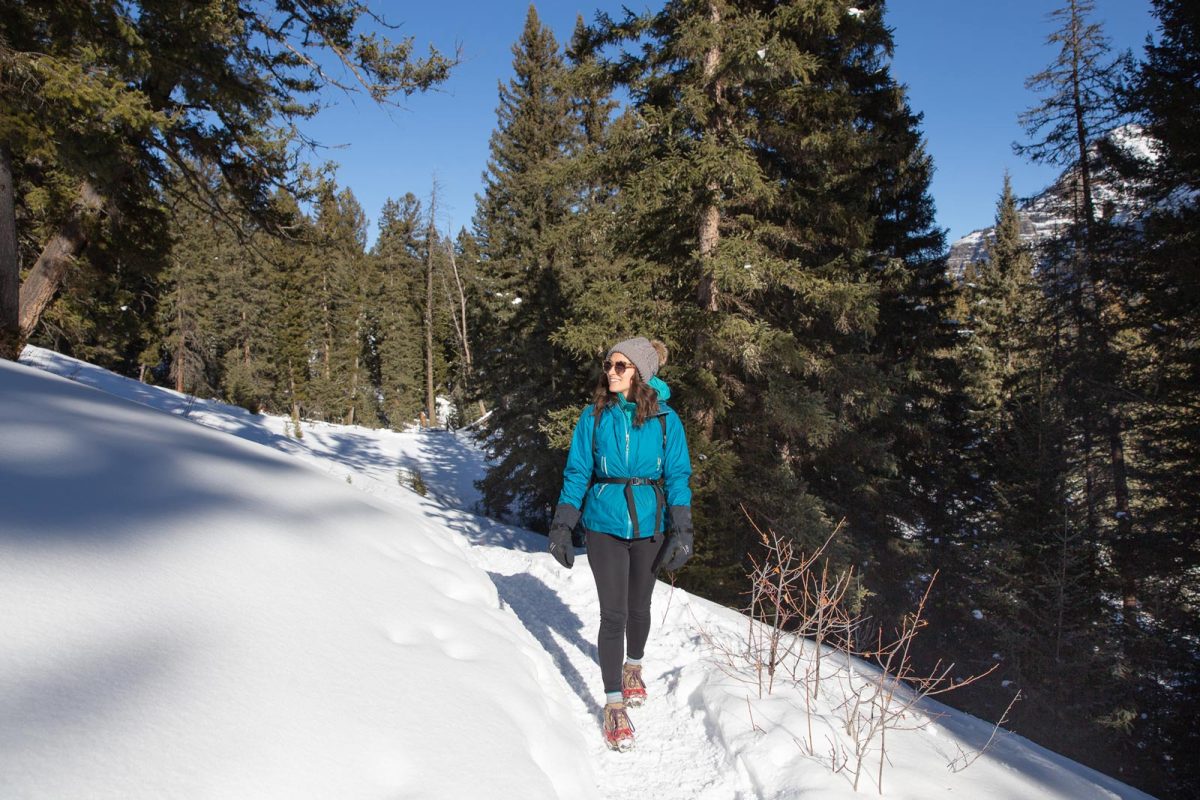 A woman in winter hiking clothing on a snow-covered hiking trail in the forest.