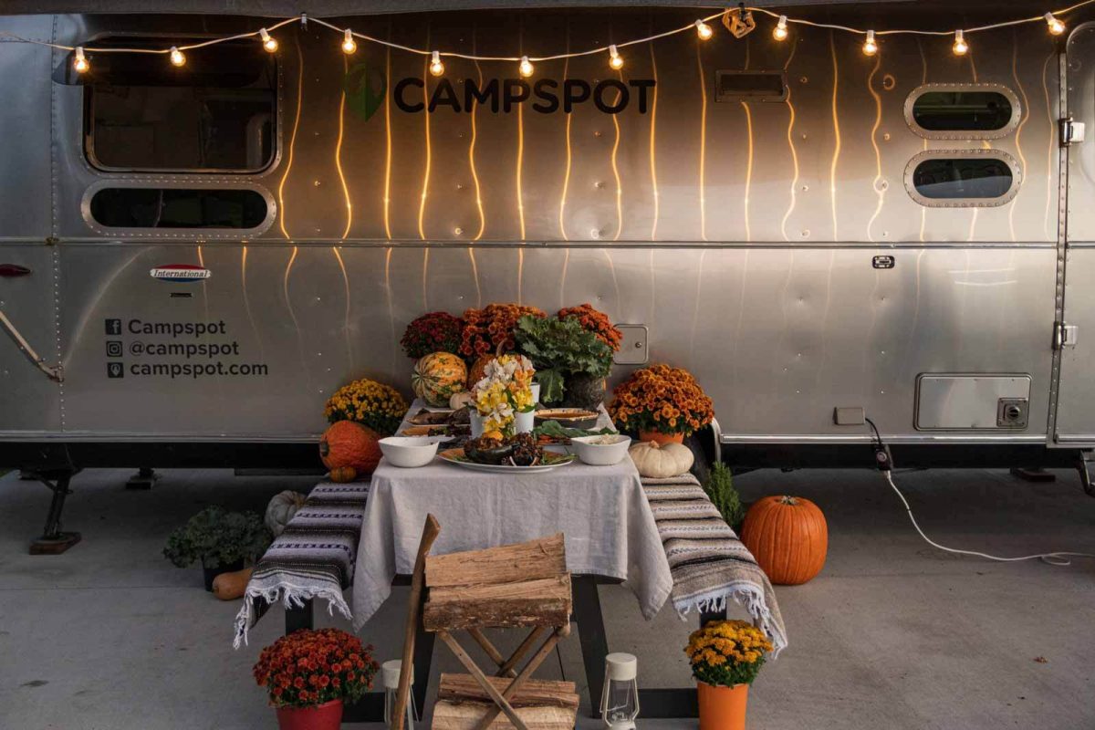 A decorative thanksgiving table is set outside of an airstream. 