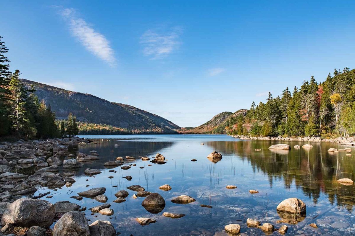 Jordan Pond in Acadia National Park. Still water between two hillsides. Rocks stick out of the water in the foreground. 