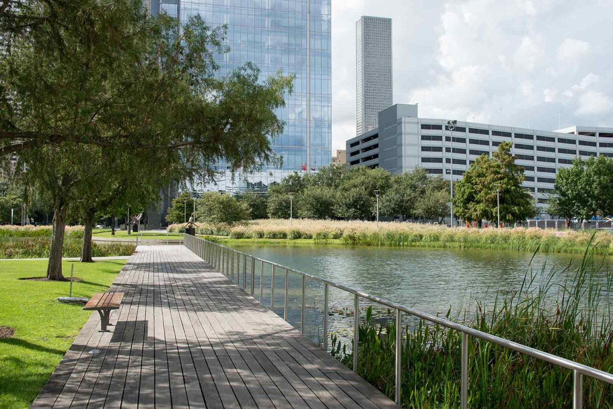 A walking trail surrounded by trees and water with Houston skyscrapers in the background. 