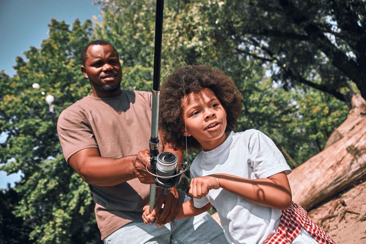 An adult helps a young child cast a line while fishing. 