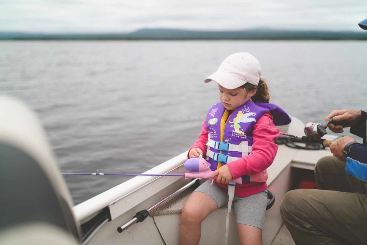 A child in a life vest holding a pink and purple fishing pole. 