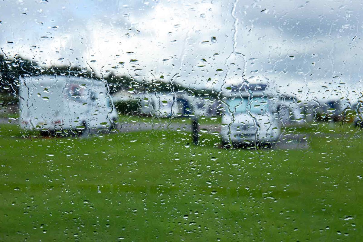 White camper vans parked in a grassy area are visible through a rain-streaked window. 