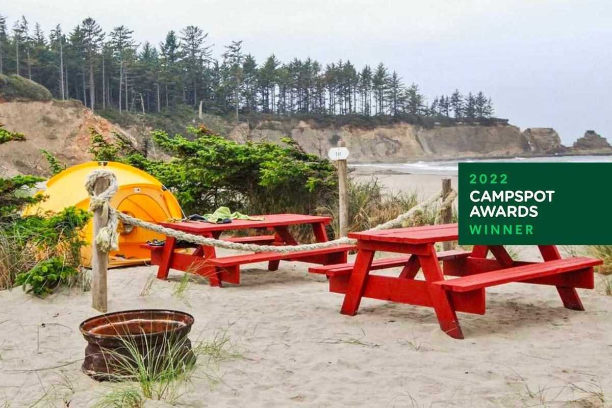 Red picnic tables and a yellow tent on the beach at Oceanside RV Resort and Campground, a campground on the water 