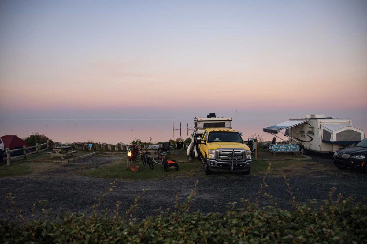 A yellow truck and a camper parked at a campground on the water. 