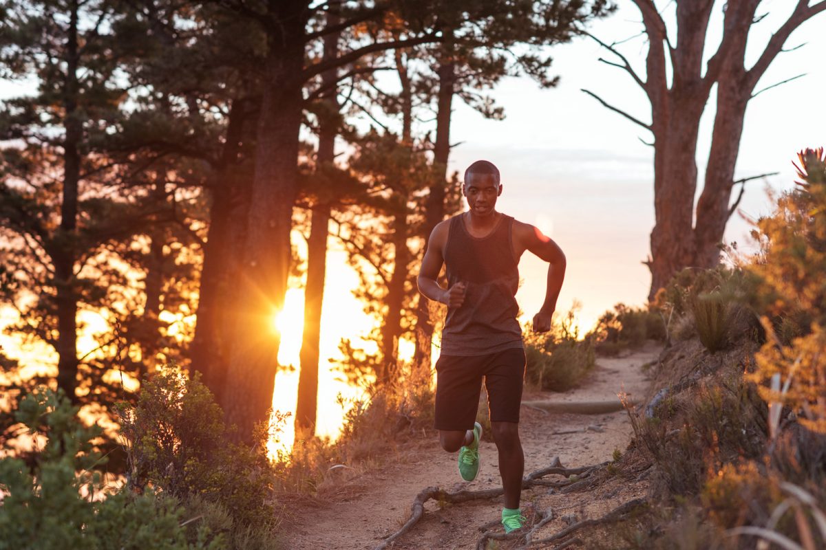 Trail runner in a tank top on a downhill trail with the sunsetting in the distance. 