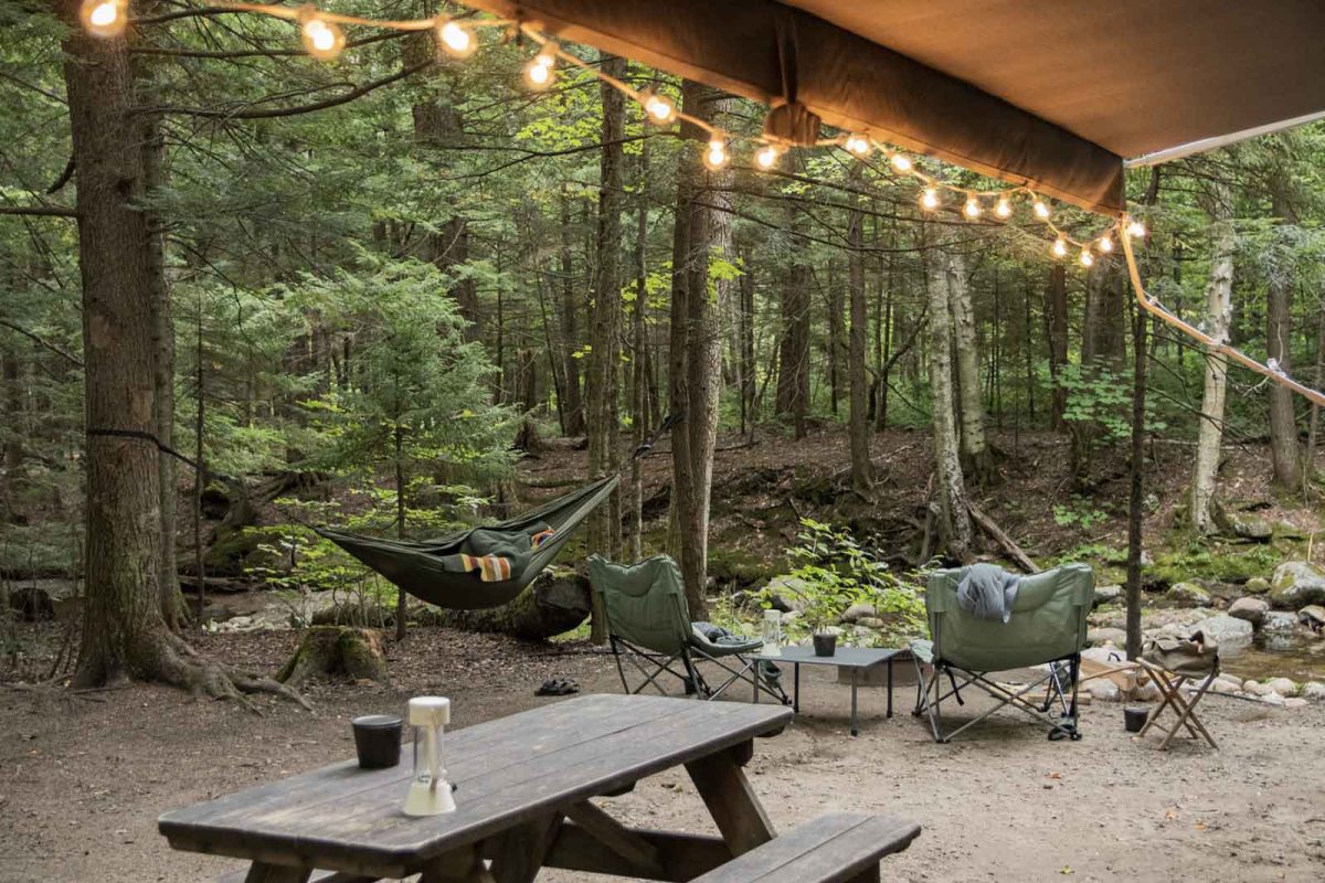 Twinkle lights hang from an RV awning with a picnic table and hammock in view. 