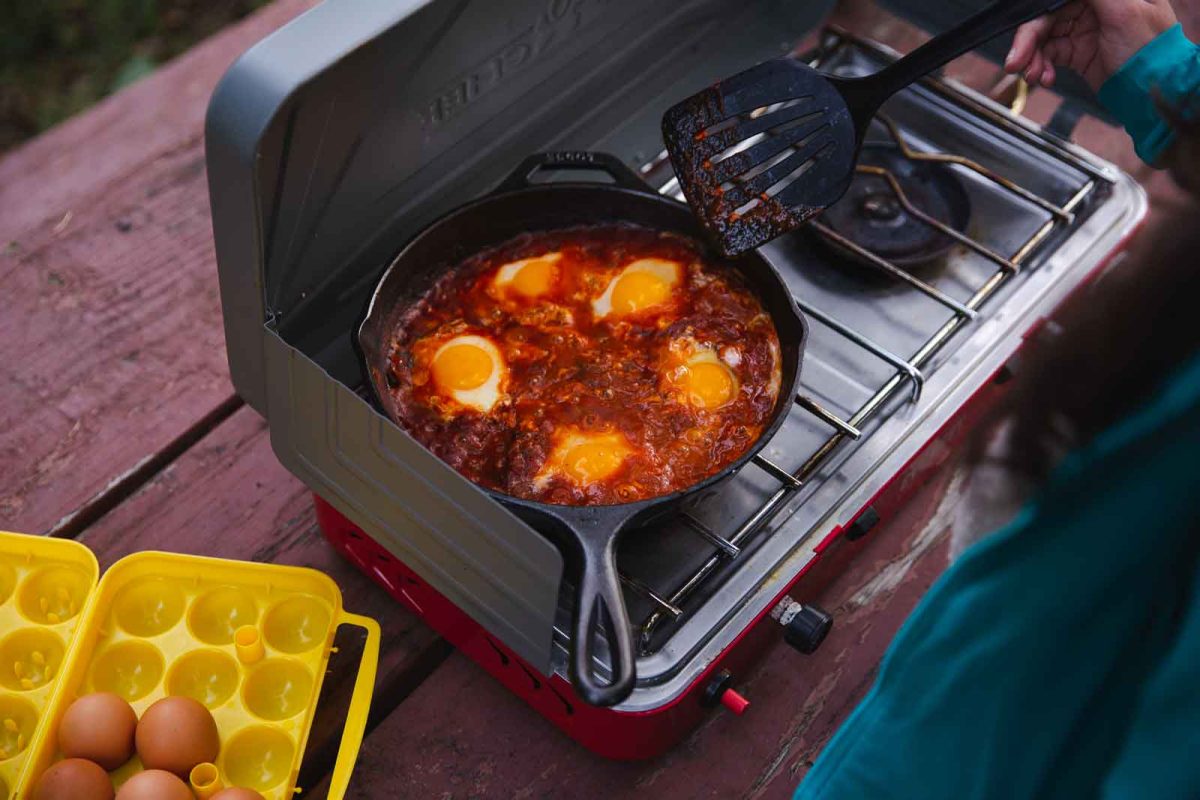 Eggs cook in tomato sauce in a cast iron skillet on a camp stove. 