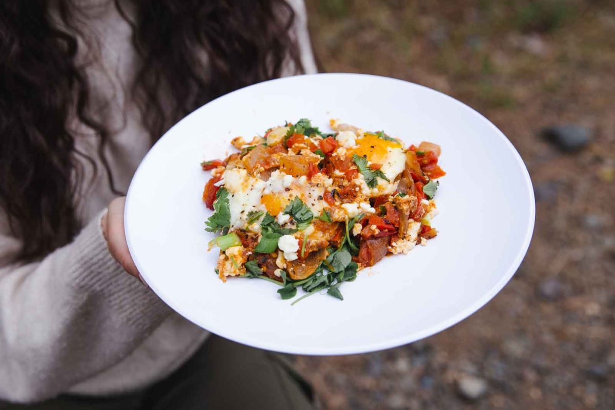 A person holds a plate of shakshuka. 