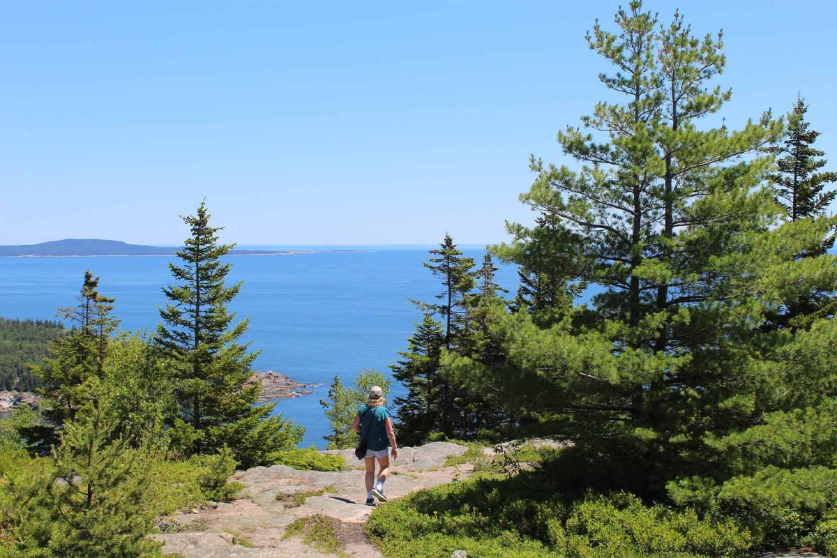 A hiker descends a rock path that overlooks the ocean on the Gorham Mountain Loop trail in Acadia National Park, one of the most popular places to go hiking in Maine, and in the country. 