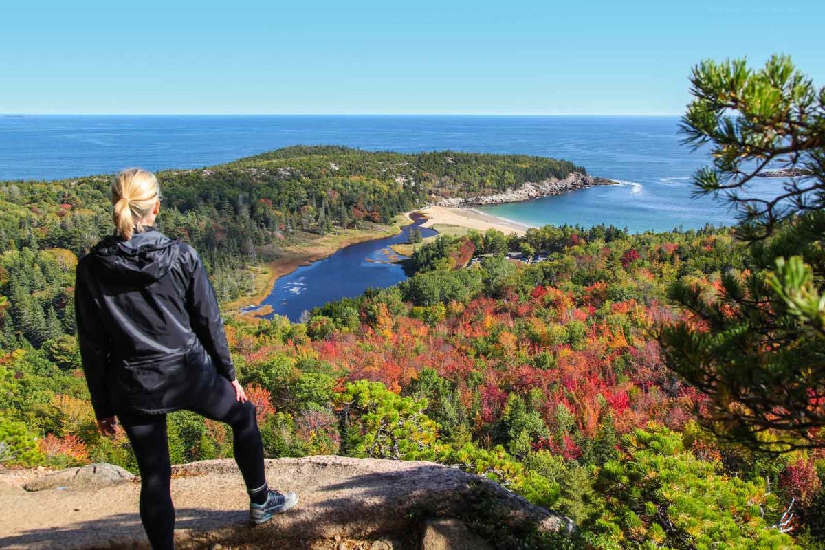 A hiker stares out at the view of the ocean and a tree-covered peninsula from her viewpoint on Beehive Loop trail, a popular place to go hiking in Maine. 