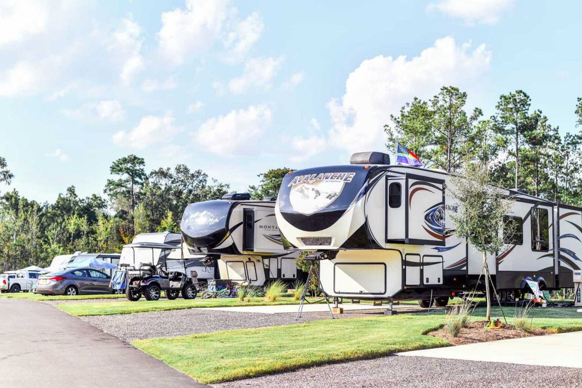 RVs parked side by side at Carolina Pines RV Resort with blue skies and clouds overhead. 