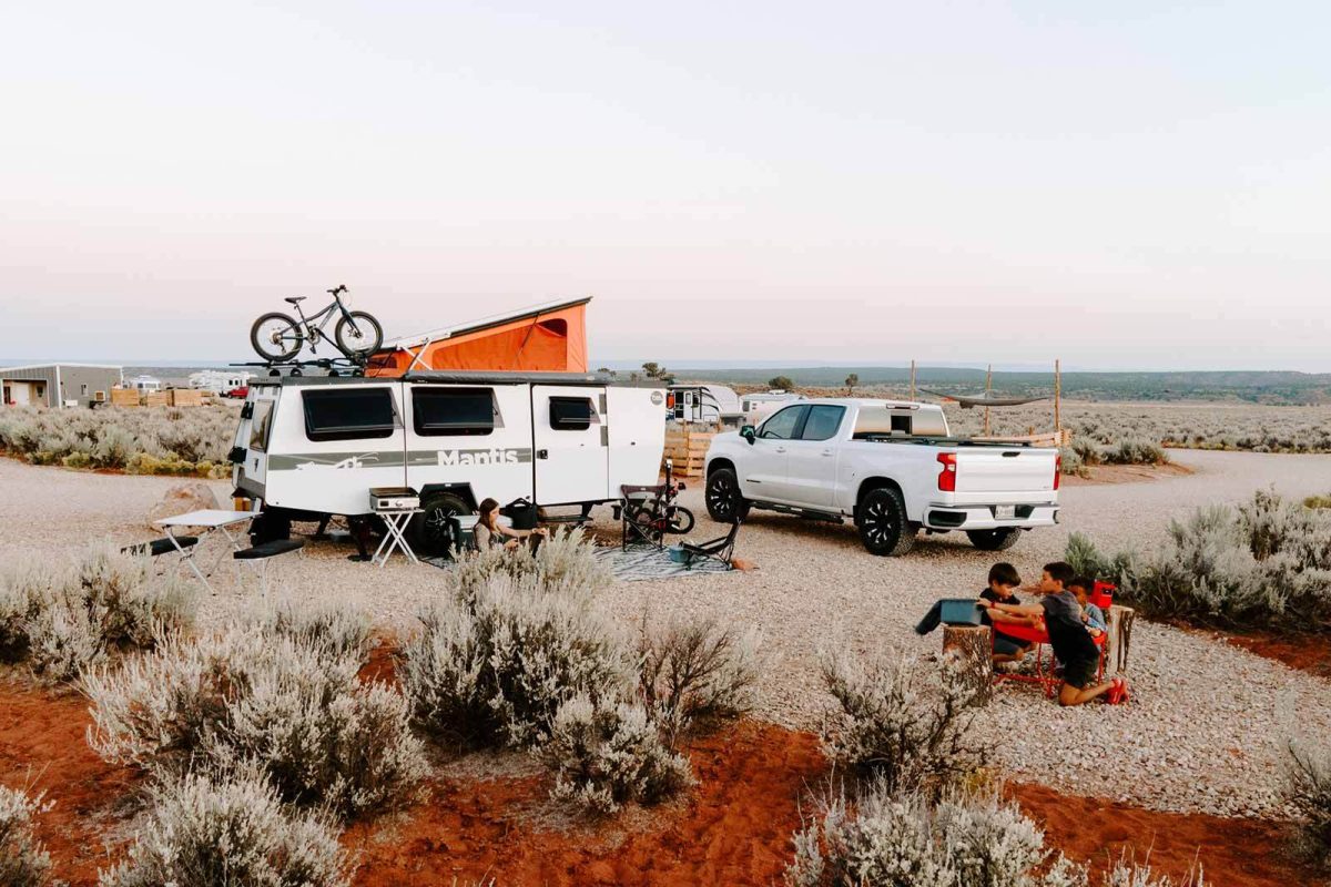 An image of an RV with a mountain bike attached to the top and a family enjoying their campsite at Dark Sky RV Campground. 