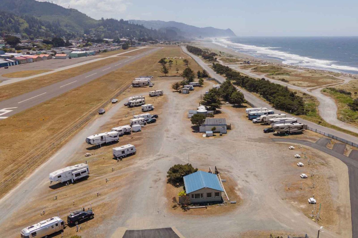 An aerial view of Oceanside RV Resort & Campground. RVs are parked in rows beside a road with the beach and ocean in the distance. 