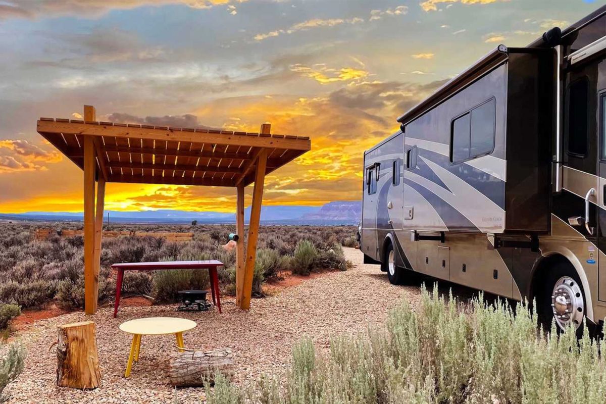 An RV parked in the desert next to a small pavilion with a picnic table with the sun setting in the distance at Dark Sky RV Campground, one of the most popular campgrounds for stargazing.  